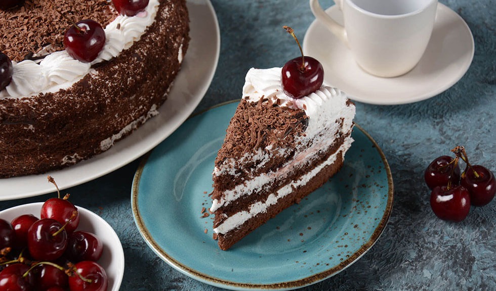 Schwarzwälder Kirsch Torte ein Stück Schwarzwälder Kirschtorte auf einem teller mit einer Tasse und einem Schälchen mit frusachen Kirschen