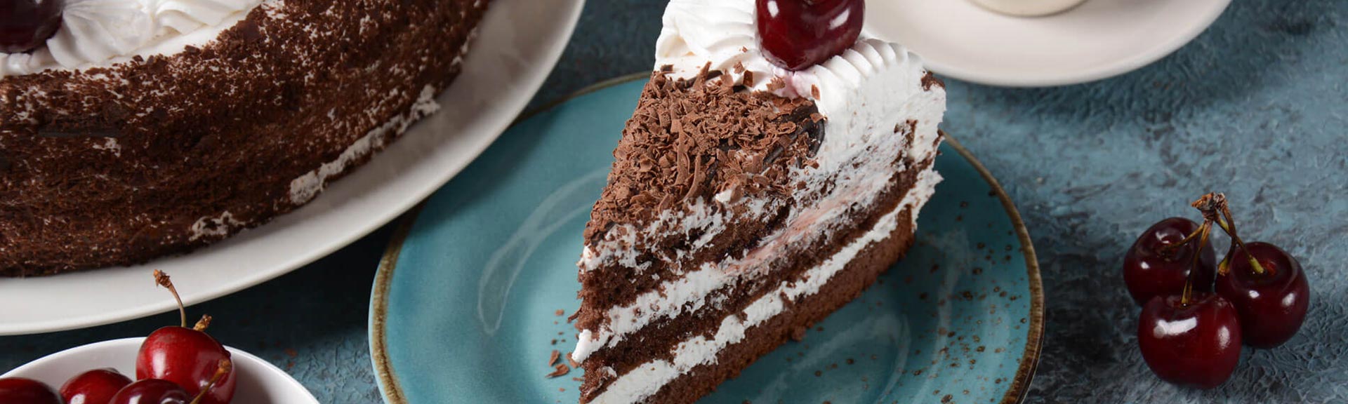 a piece of black forest cake on a plate with a cup and a small bowl with frusache cherries