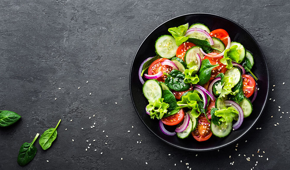 frischer Salat Gesunder Gemüsesalat aus frischen Tomaten, Gurken, Zwiebeln, Spinat, Salat und Sesam auf dem Teller.
