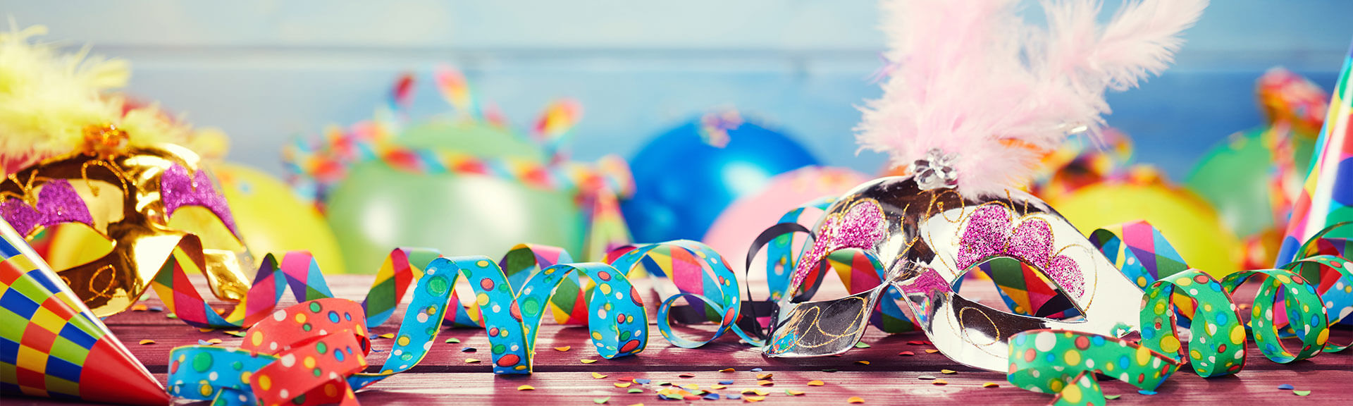 fasching Landgasthof zur Blume Farbiges Karnevals Panoramabanner mit Partyballons Luftschlangen Hüten Maske und Konfetti auf einem Holztisch
