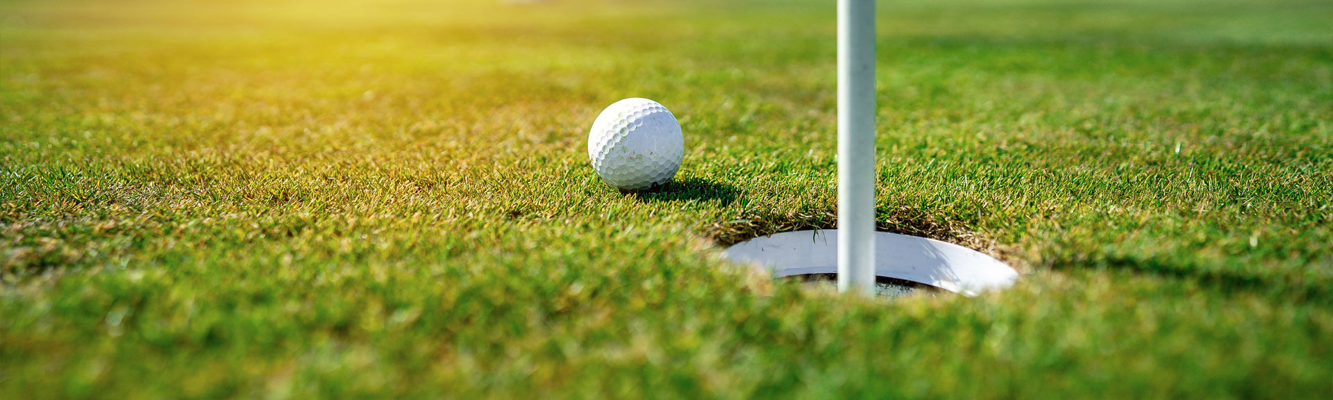 Closeup eines Golfball vor einem Loch mit einem Golfspieler im Hintergrund