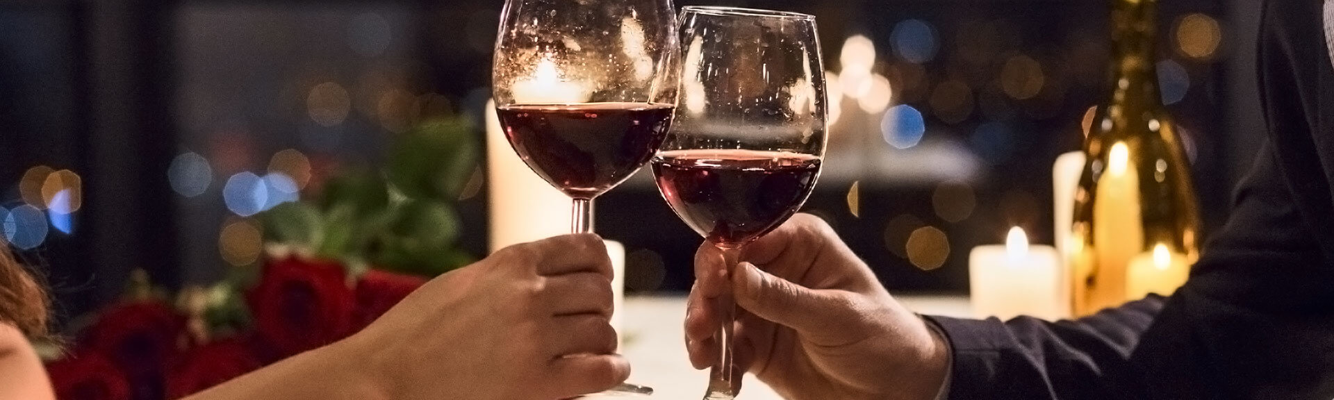 2 people at a candlelight dinner in a restaurant toast with red wine glasses